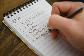 Hand holding a pencil writing a list of daily gratitude on a notepad